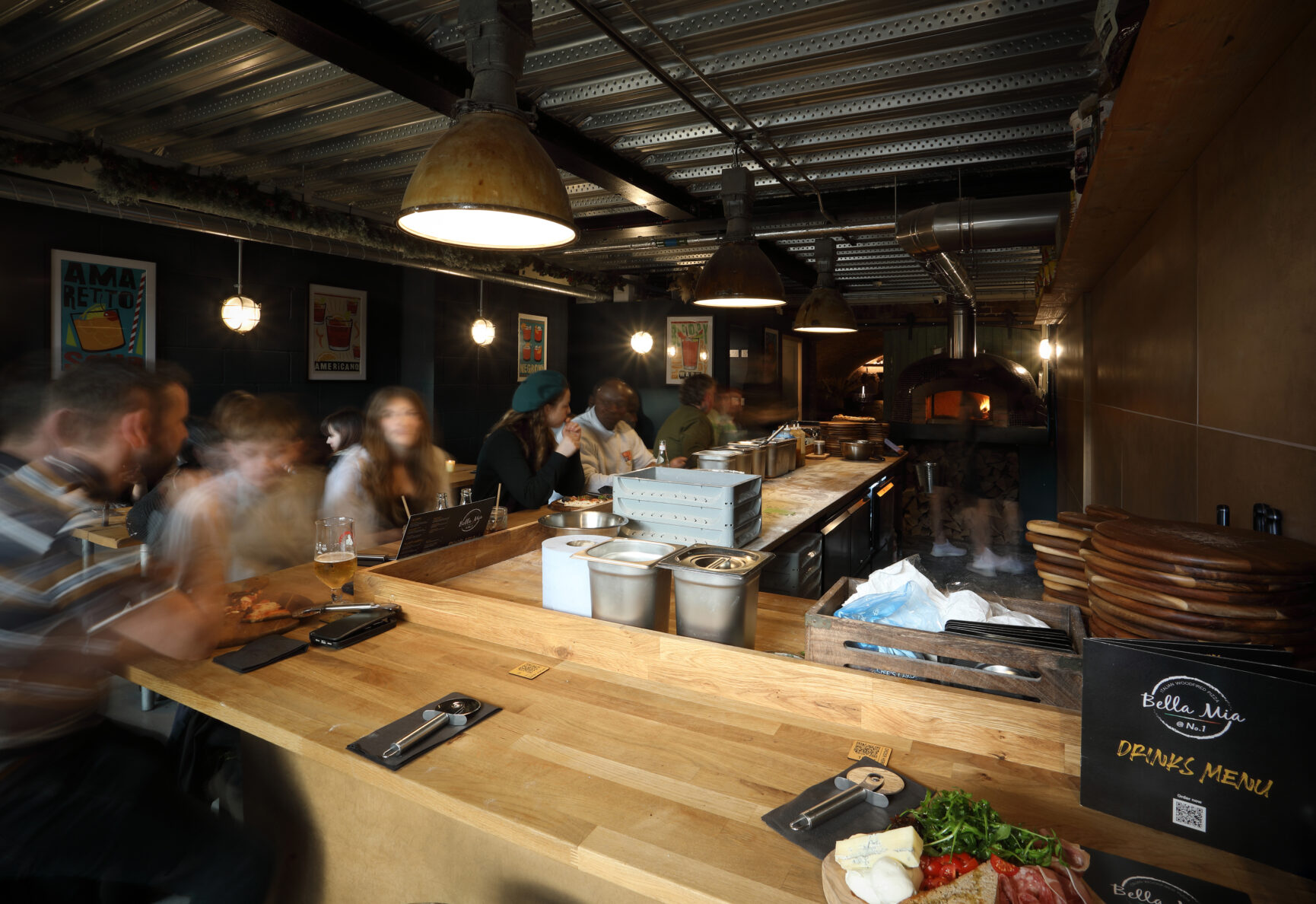 A group of customers seated at the wooden bar that faces the Bella Mia Pizza kitchen.