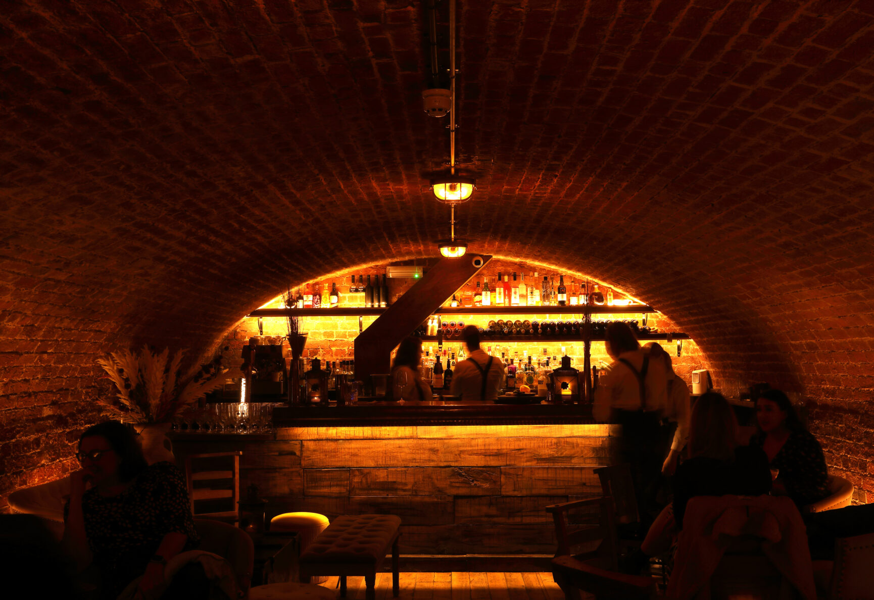 A low-light photo of the GreenDoor bar. Tables and chairs sit in front of the semi-circle vaulted ceiling, with a built in bar on the back wall.