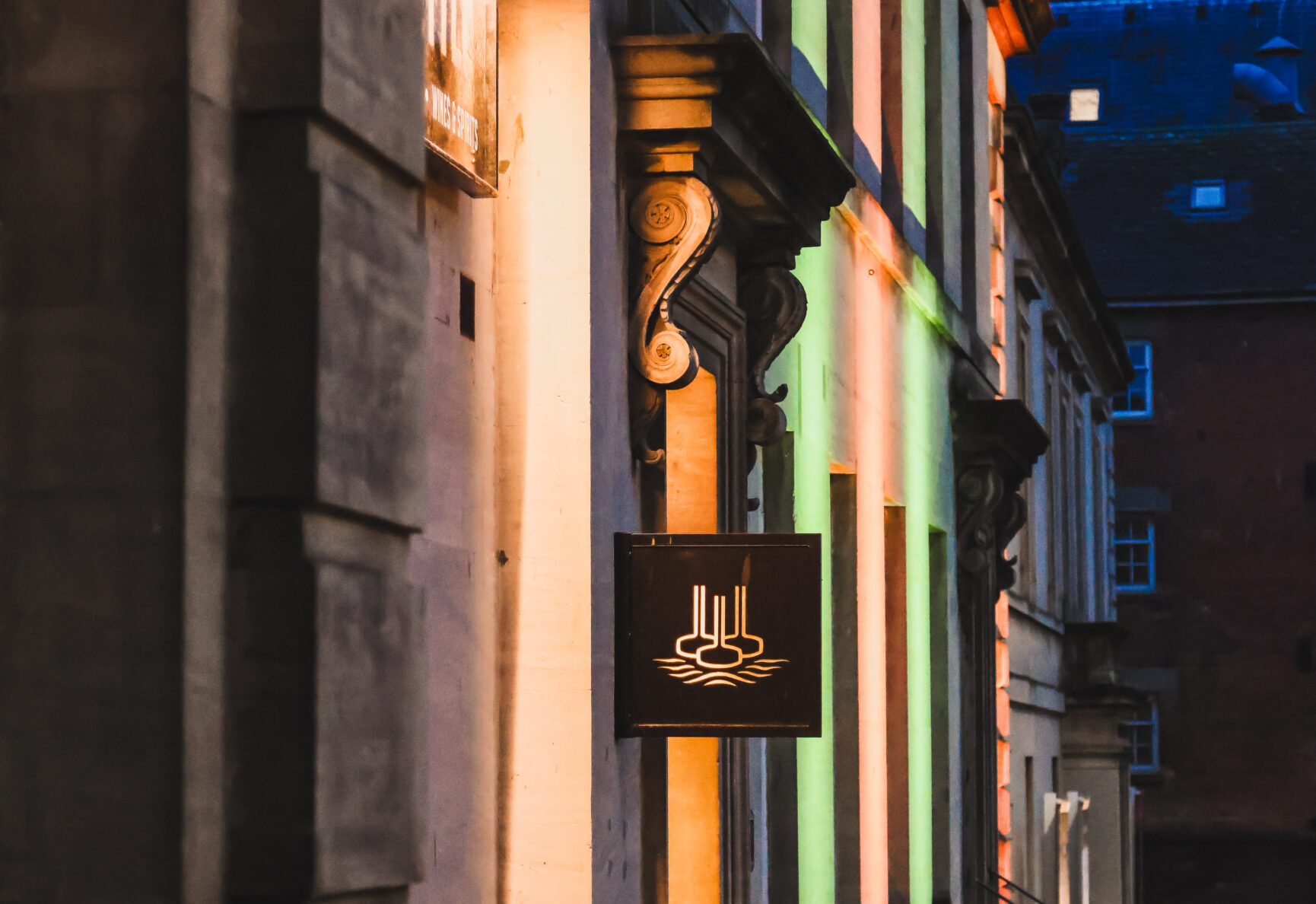 Hop Kettle's entranceway on Commercial Road. It's dusk and the sky is a deep blue. Red, green and gold lights shine on the stonework of the building.