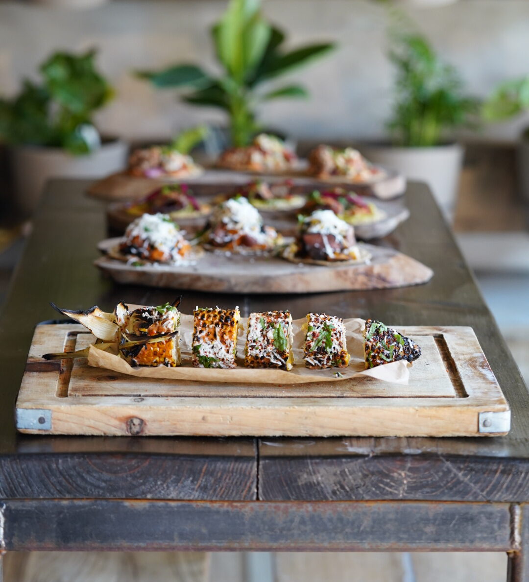 Three dishes in a row on a wooden table in Elote, with their classic 'Elote' corn at the front.