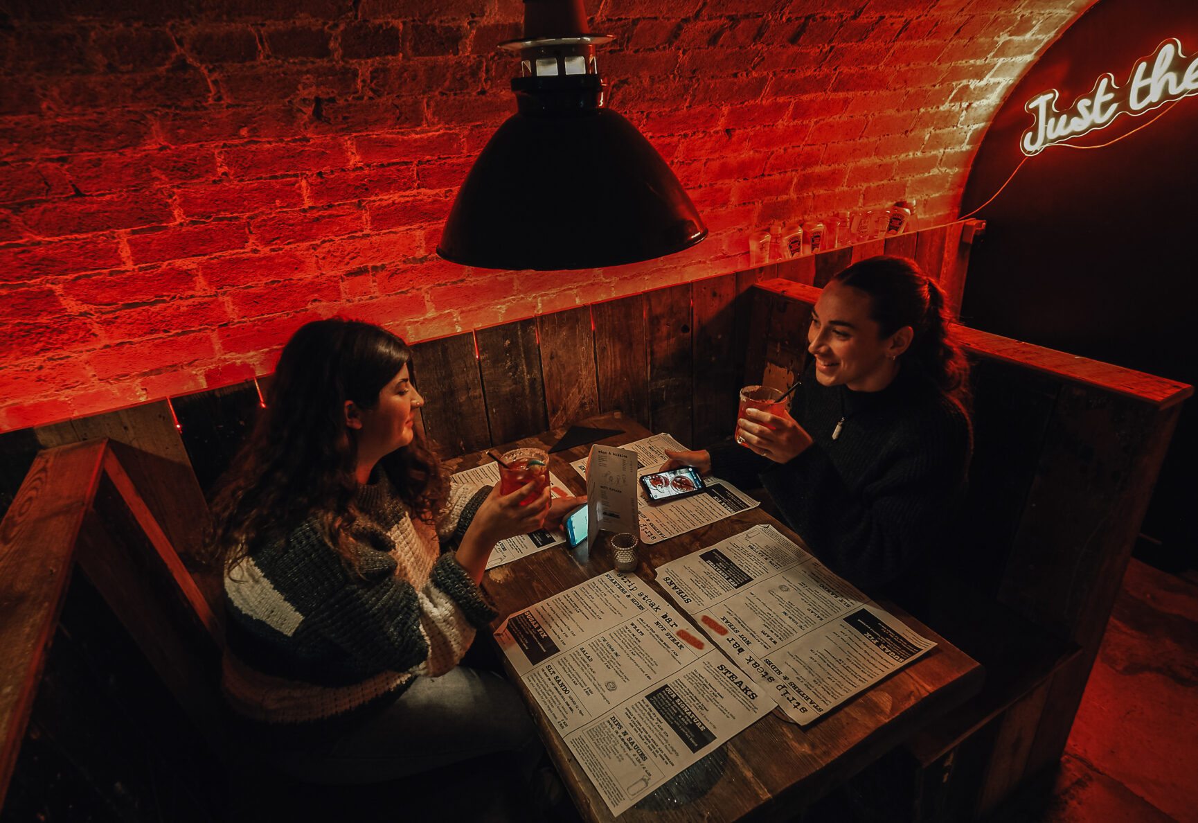 Two friends sat in a cosy booth at Strip Steak with cocktails.