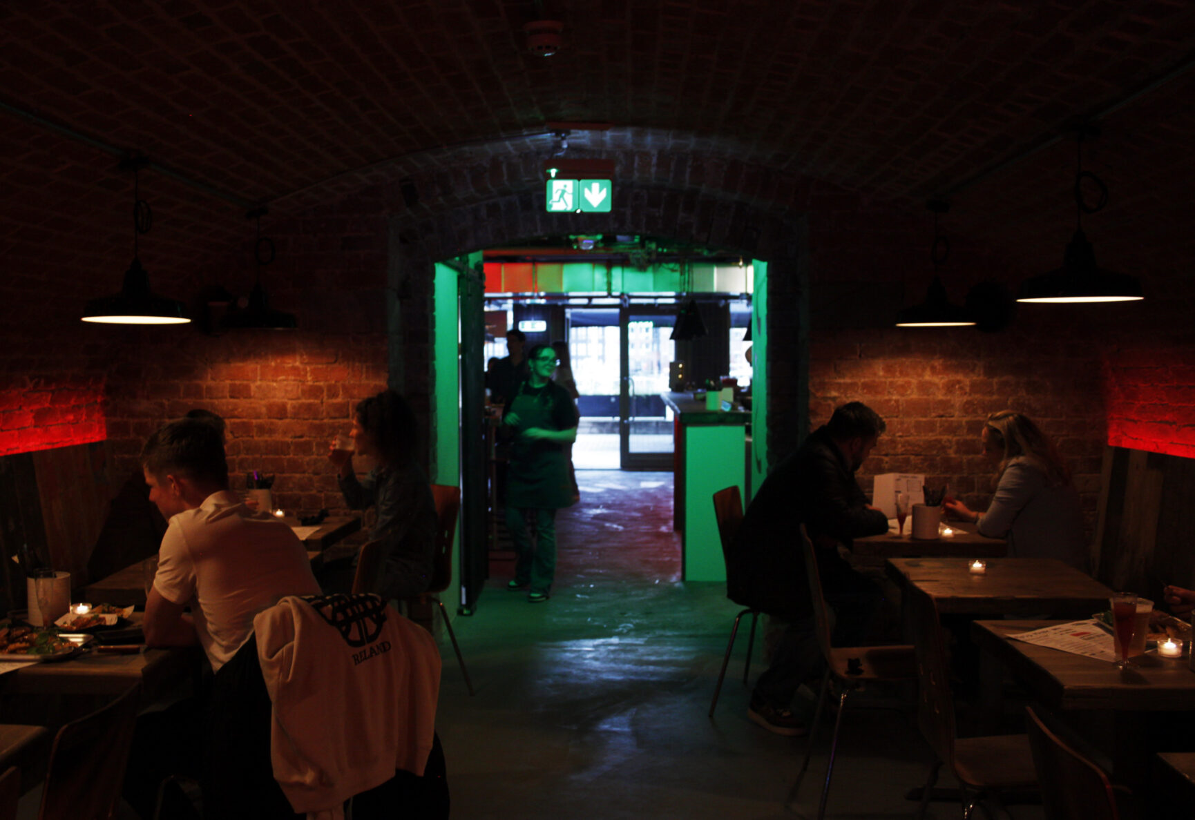 Looking from the back of Strip Steak towards the entrance. The tables have a warm glow, with the middle of the bar glowing green from a neon green sign.