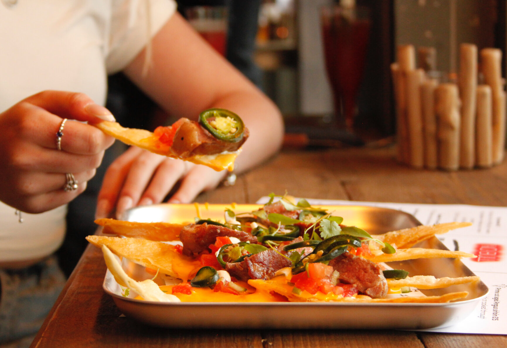 A serving of loaded Strip Nachos, with jalapenos tortilla chips, salsa, and smoky sour cream.