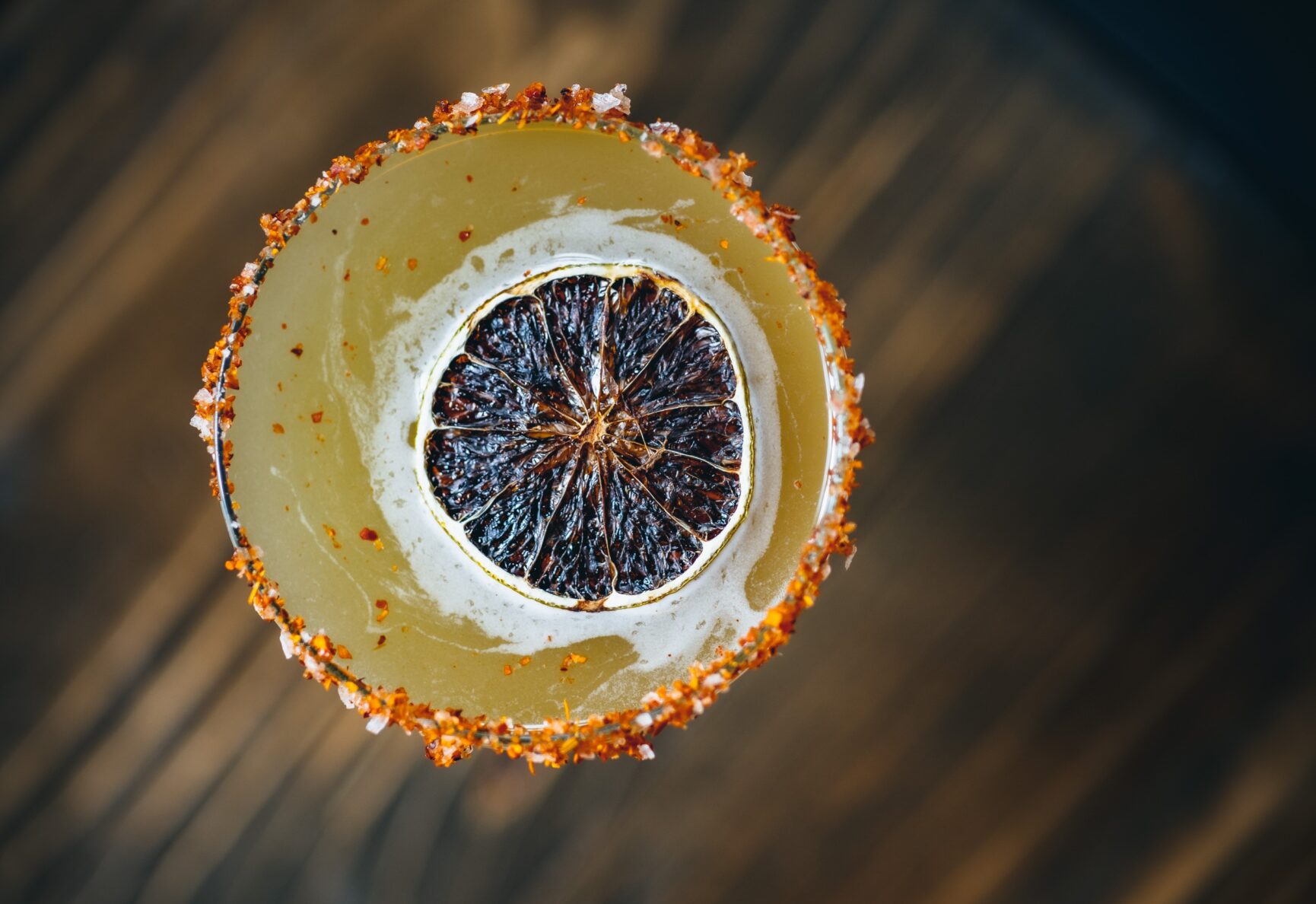 Looking down on one of Elote's margarita cocktails. It is yellow, with a dried orange wedge as a garnish.