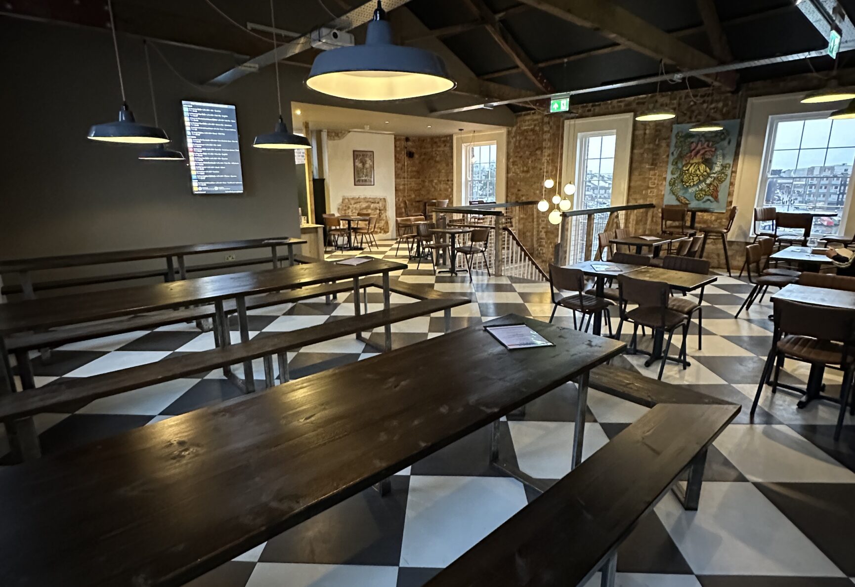 An view of the open plan room upstairs in Hop Kettle. The place where pub quizzes are held. There are long wooden tables and benches, and groups of other smaller tables.