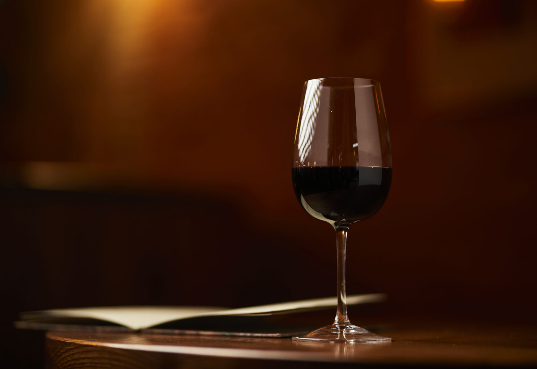 A glass of red wine on a wooden table with a menu next to it.