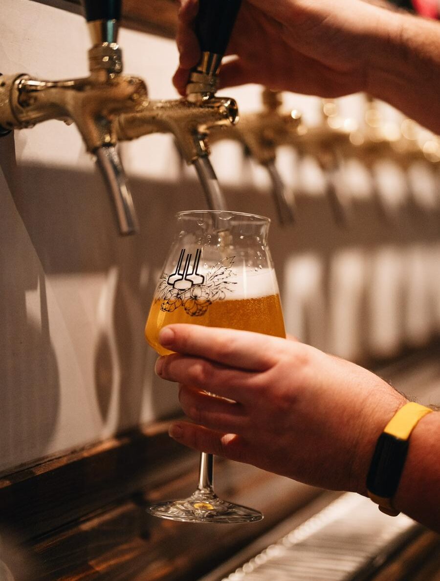 A hand holds a goblet glass to a gold tap to pour a pint.