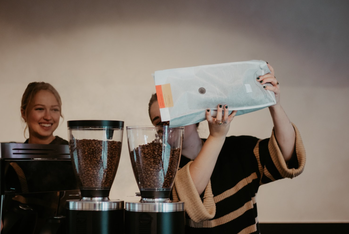 Owner Sophie smiling as a barista refills the coffee beans.