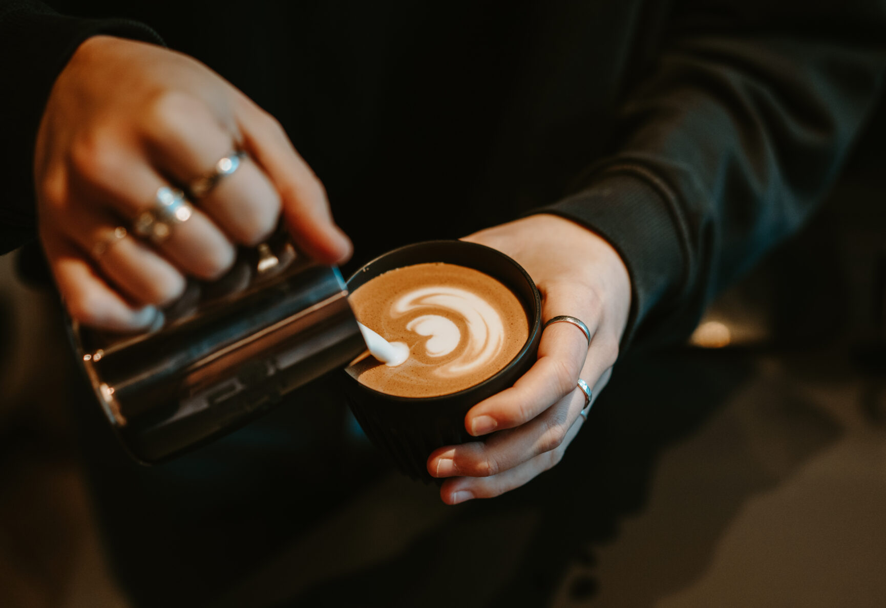 Milk carefully being poured into a coffee cup.