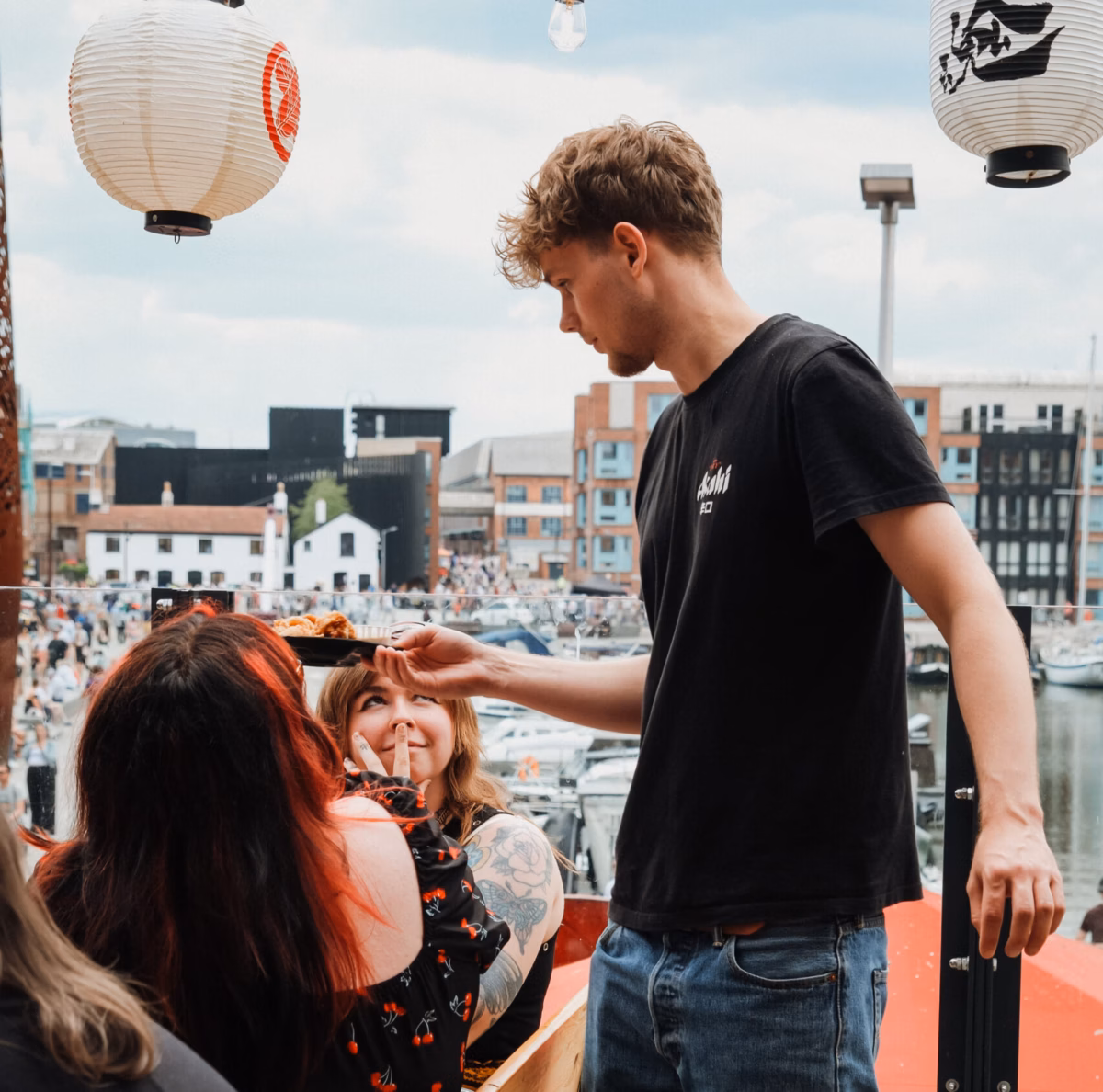 Daikoku team serving up authentic Japanese dishes with a smiling customer and a view across the Victoria Quay in the docks.