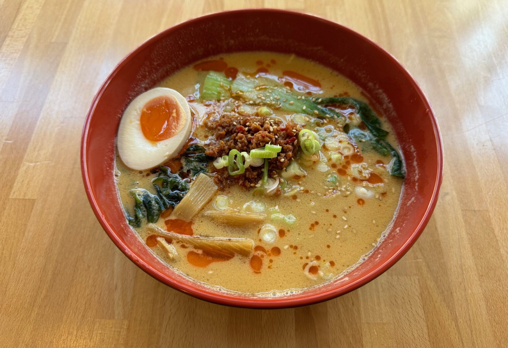 A bowl of Ramen, with fresh greens, pieces of ginger, an egg and other toppings.