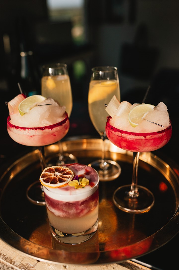 A selection of red cocktails and flutes filled with fizz on a bronze metal serving tray.