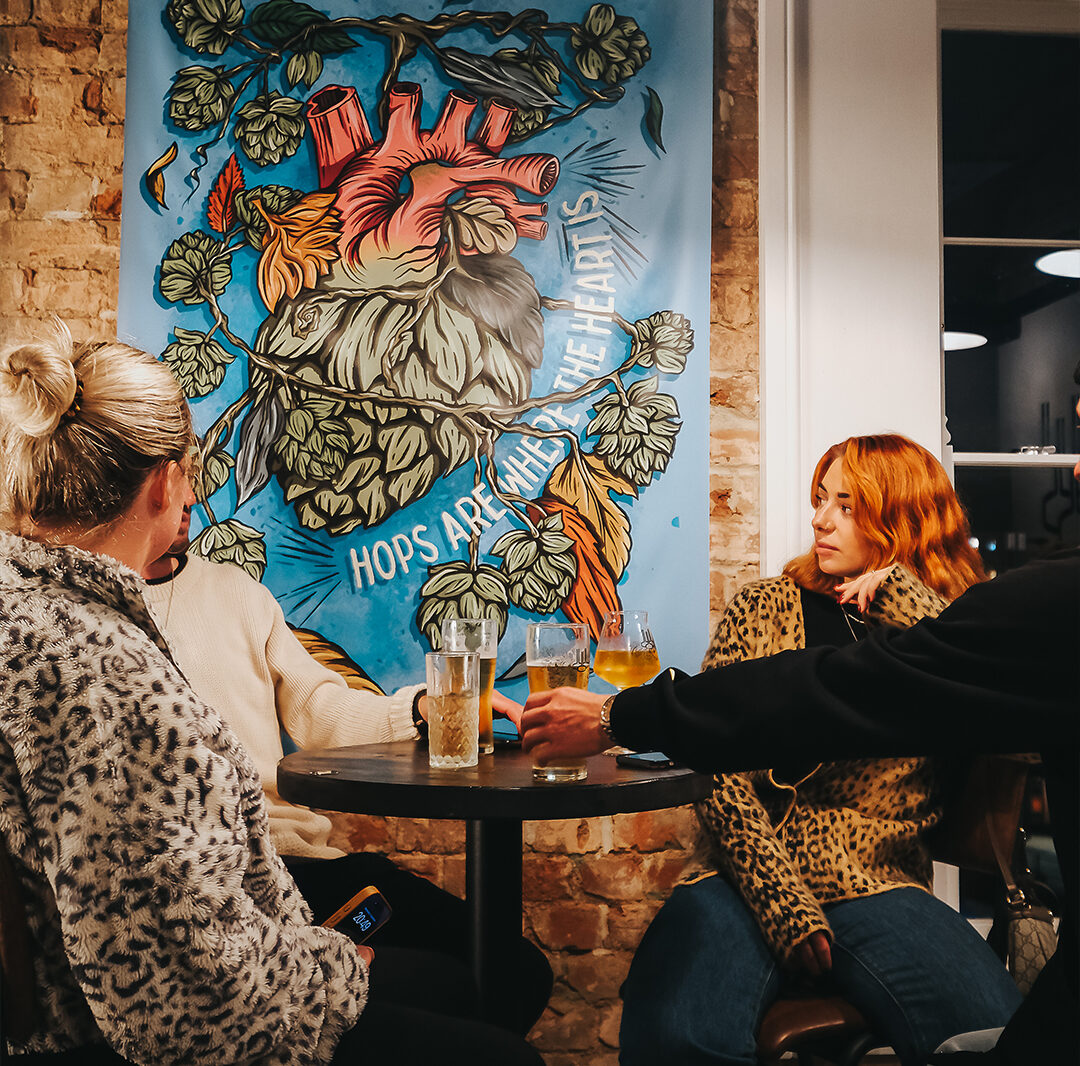 A group of friends sits at a high table in Hop Kettle, with a beers on the table. Everyone is wearing a cosy jumper.