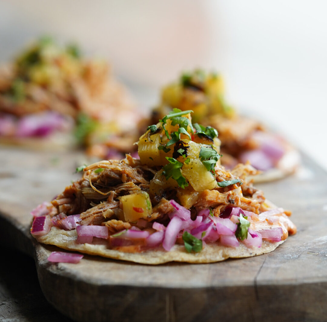Three colourful, open tacos on a wooden board.
