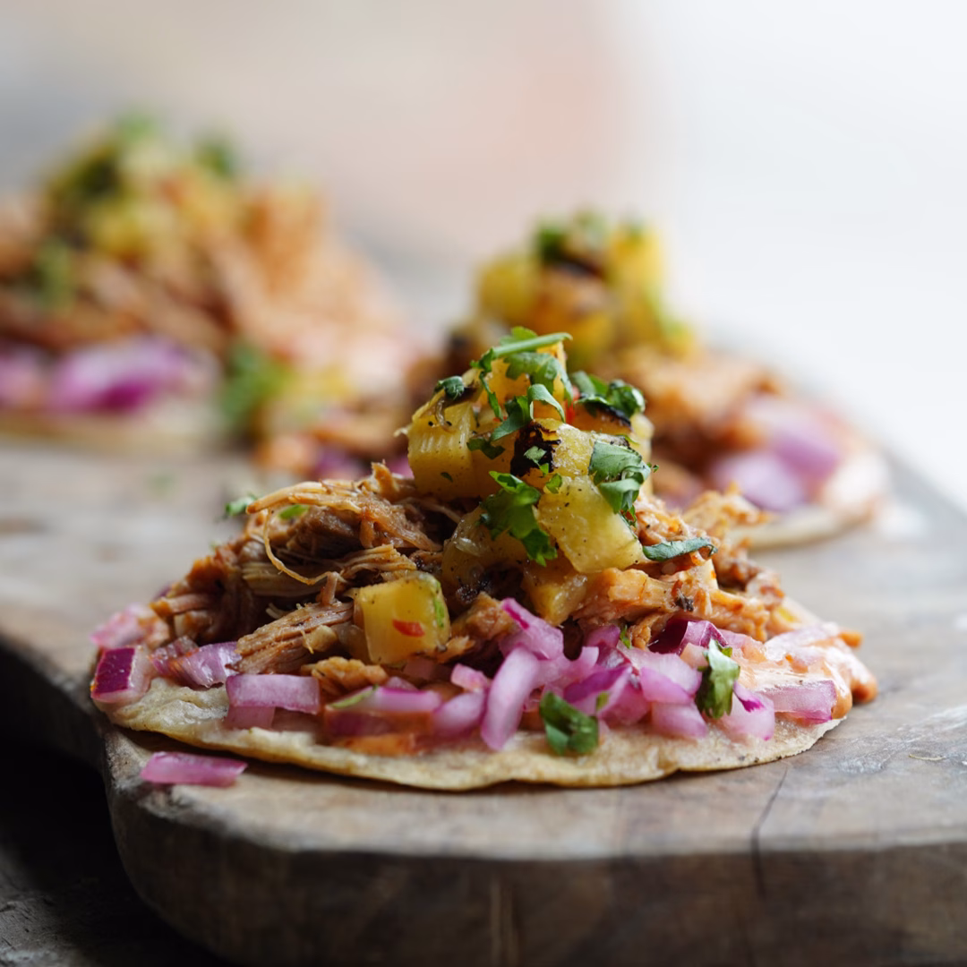 Three colourful, open tacos on a wooden board.