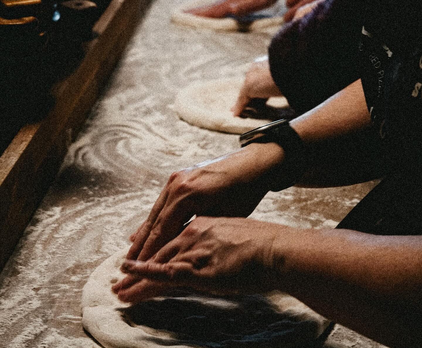 A close up of a row of hands working the dough.