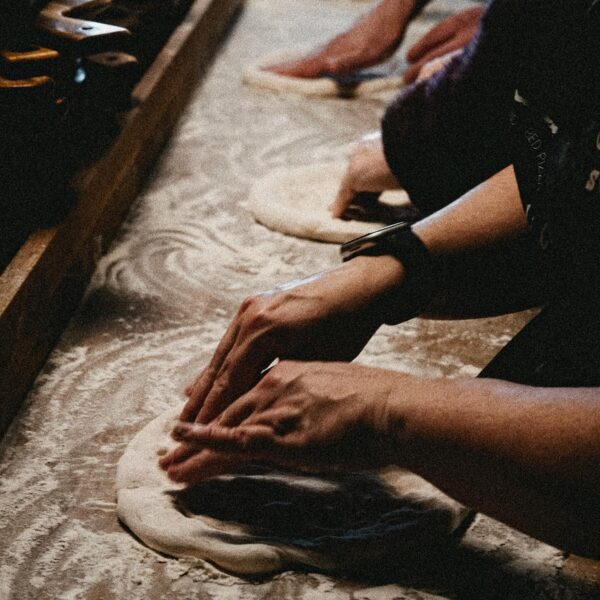 A close up of a row of hands working the dough.